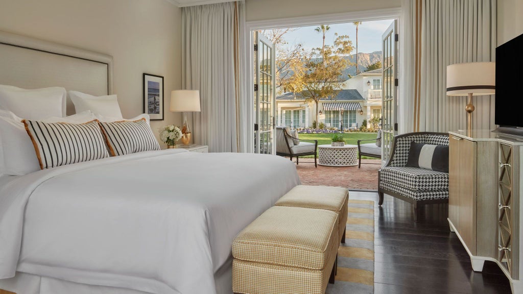 Spacious garden bungalow suite with elegant coastal California decor, featuring plush white bedding, wooden floors, and private outdoor seating area.