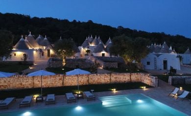 Rustic stone trullo houses at luxurious Scenset Borgo nestled in Puglia's countryside, with warm golden sunlight and lush green surroundings