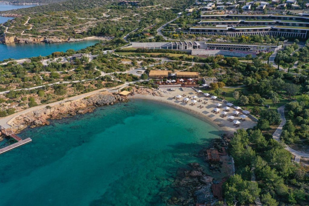 Modern Mediterranean resort nestled into coastal cliffs, featuring infinity pools overlooking turquoise Aegean Sea at sunset