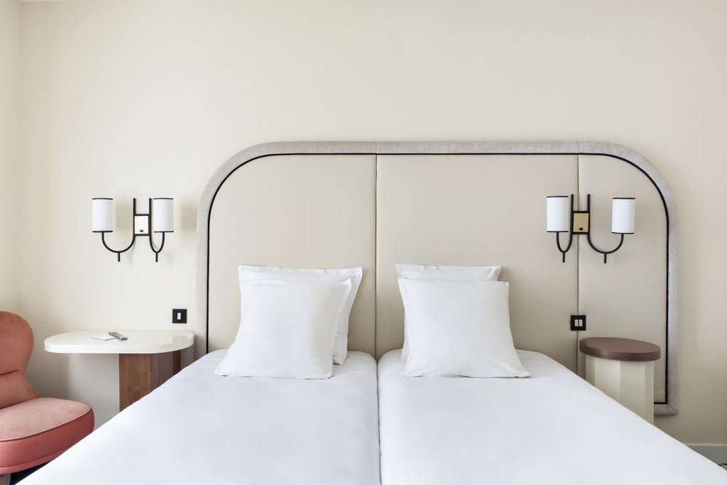 Elegant twin room at Hôtel Bienvenue with plush white bedding, soft neutral tones, vintage-inspired decor, and warm ambient lighting in Paris