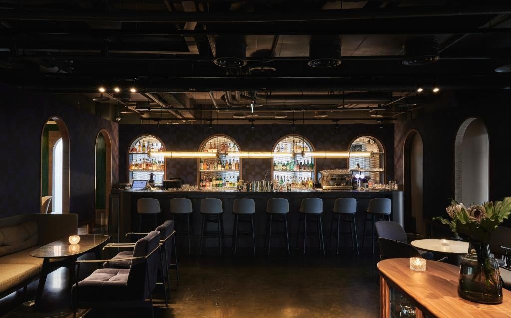 Sleek modern hotel facade with floor-to-ceiling windows, geometric patterns, and warm lighting illuminating the contemporary exterior at dusk