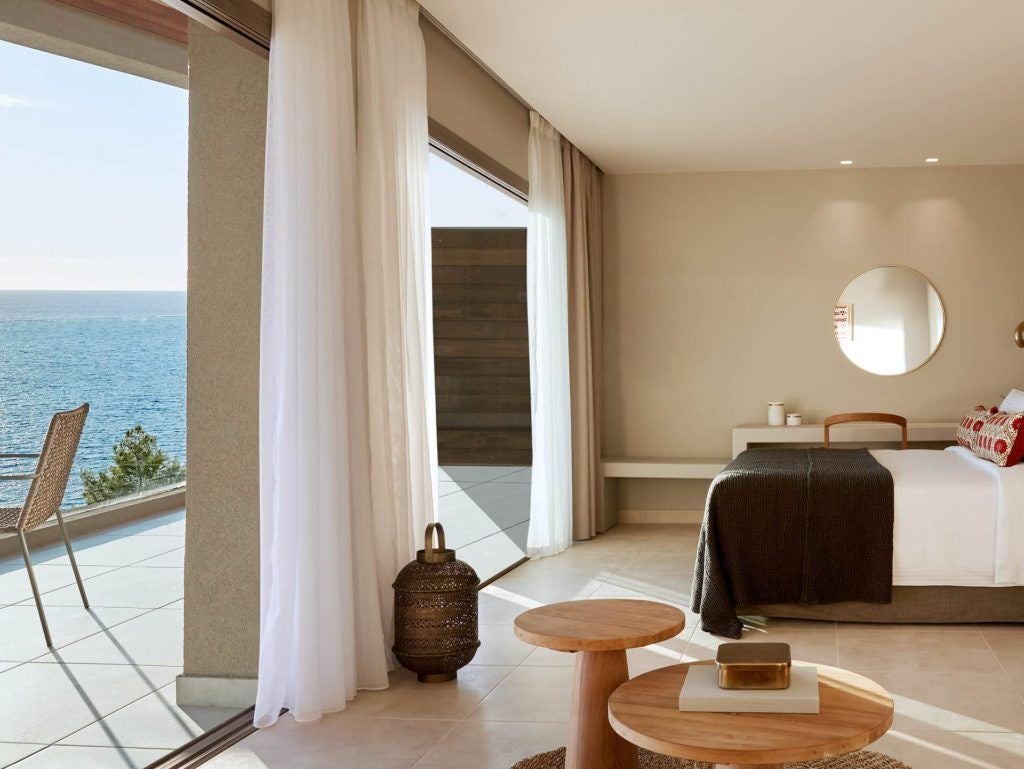 Luxurious junior suite at Elix hotel with expansive sea view, modern minimalist design, white-toned decor, and panoramic Grecian coastline through floor-to-ceiling windows