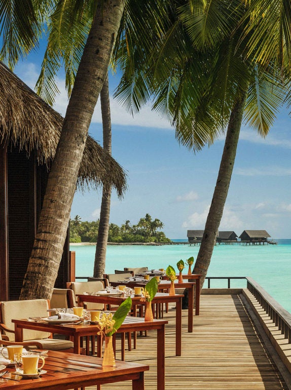 Luxurious overwater villa with infinity pool overlooking turquoise Maldivian lagoon, surrounded by palm trees at sunset