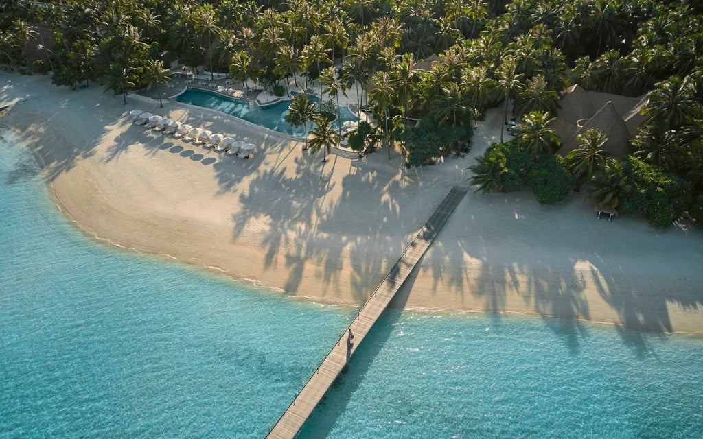 Overwater luxury villas with private pools stretch along wooden walkways above turquoise Maldivian lagoon at sunset