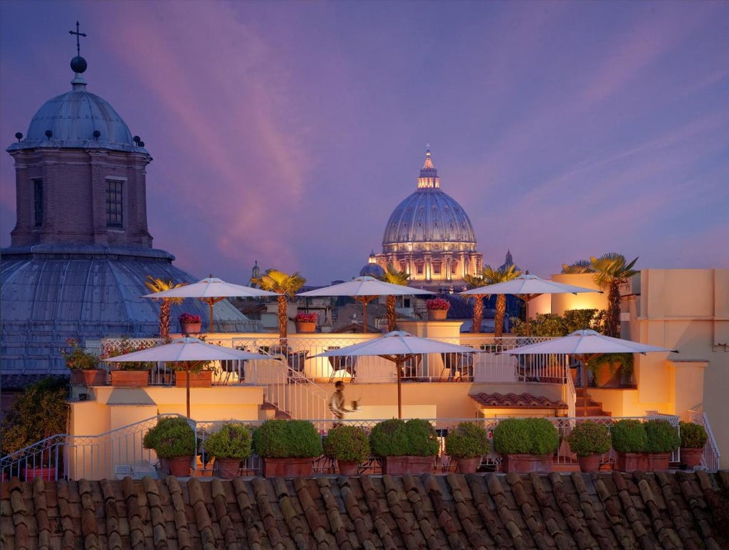 Elegant rooftop terrace of Bio Hotel Raphael in Rome, featuring ornate balustrades, lush potted plants and panoramic city views at sunset