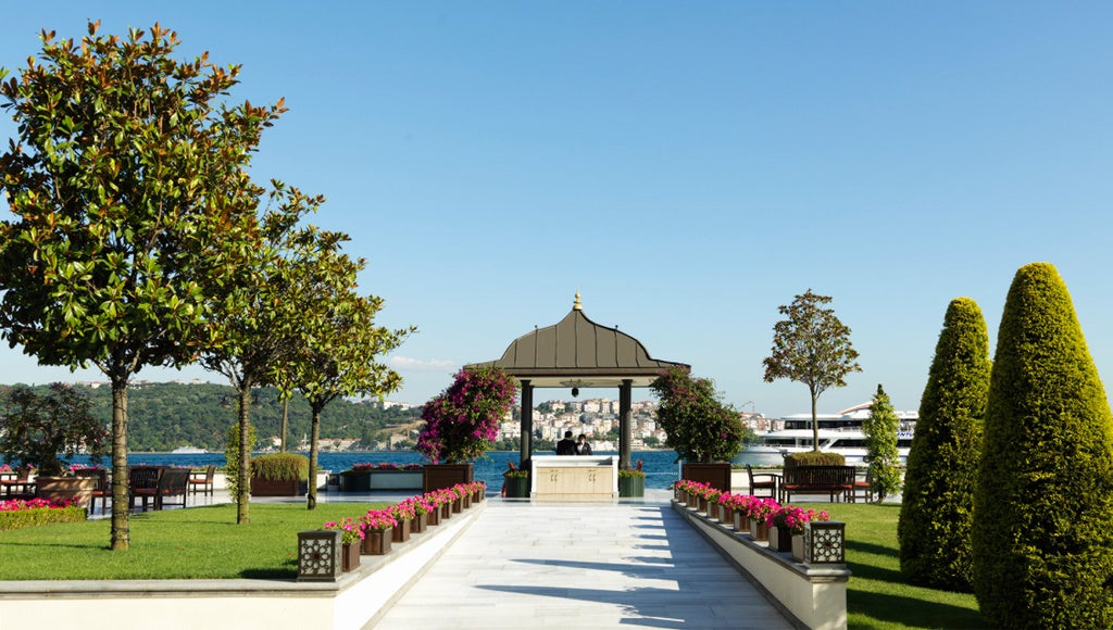 Luxurious white palace-style hotel on Bosphorus waterfront with manicured gardens, ornate Ottoman architecture, and terrace dining