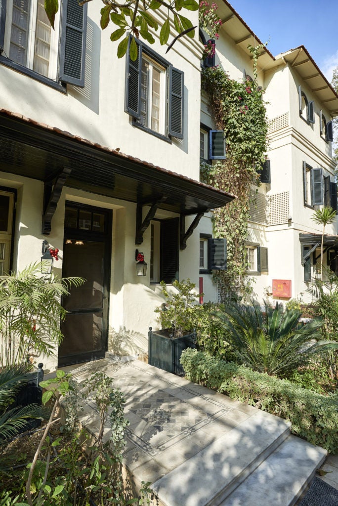 Elegant colonial-style villa with white facade, arched windows and wooden shutters surrounded by lush palm trees in Cairo suburbs