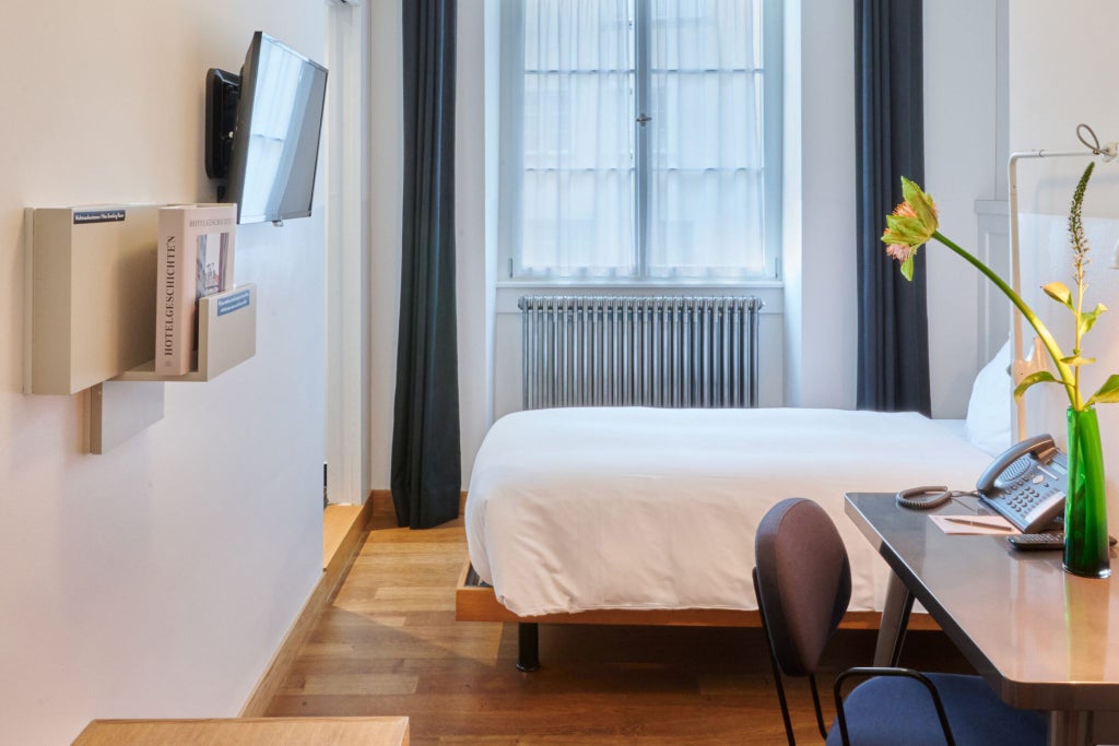 Minimalist Swiss hotel room with crisp white linens, modern wooden furnishings, large window, and elegant neutral color palette in urban boutique setting