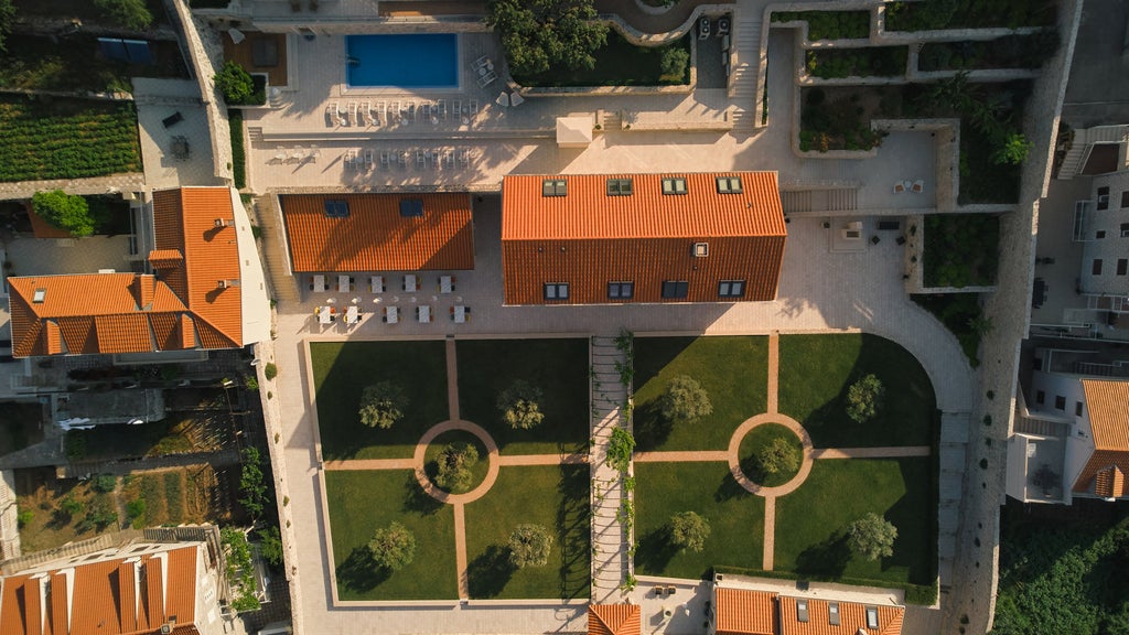 Elegant beachfront hotel with glass balconies and palm trees, overlooking crystal-clear Adriatic waters and private sandy beach at sunset