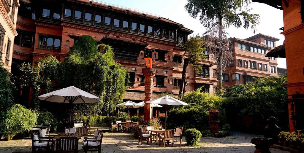 Traditional Nepali architecture with ornate wooden carvings adorns luxury hotel courtyard featuring red brick walls and peaceful garden