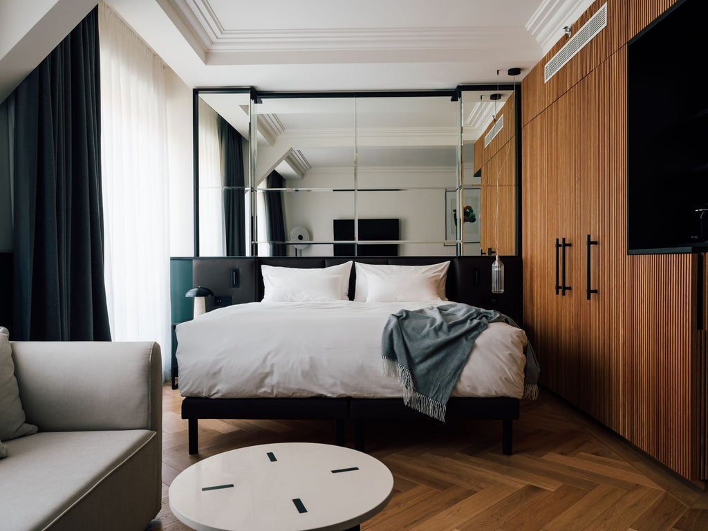 Elegant junior suite with plush white bedding, contemporary Czech design, warm wood accents, and city view in the luxurious Almanac X Alcron Hotel, Prague