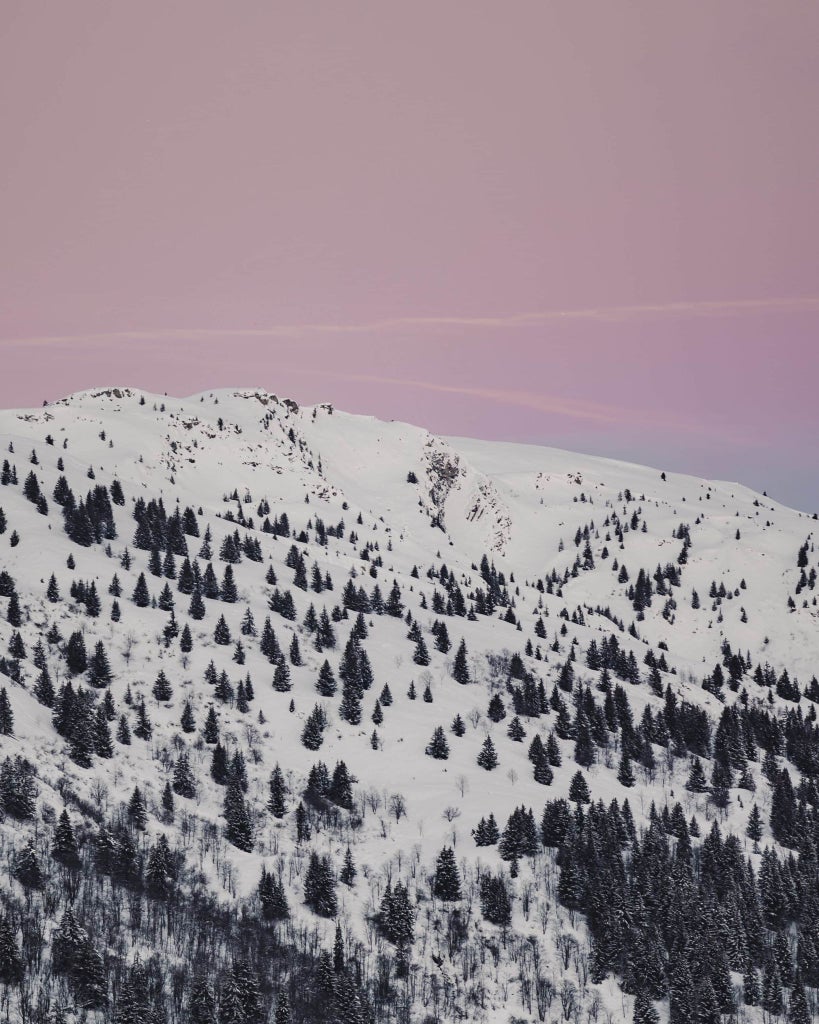 Luxurious alpine chalet-style hotel with snow-covered peaks, modern wood and glass exterior, nestled in picturesque Méribel mountain landscape at sunset