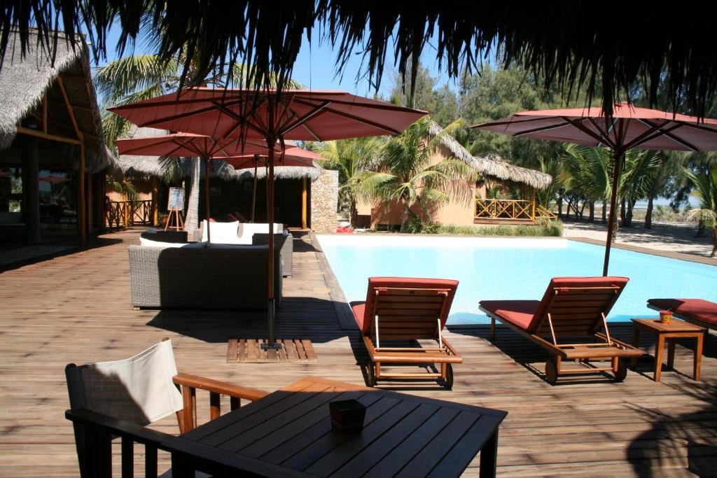 Elegant beachfront hotel with thatched-roof villas overlooking the turquoise Madagascar coast, palm trees framing infinity pool at sunset