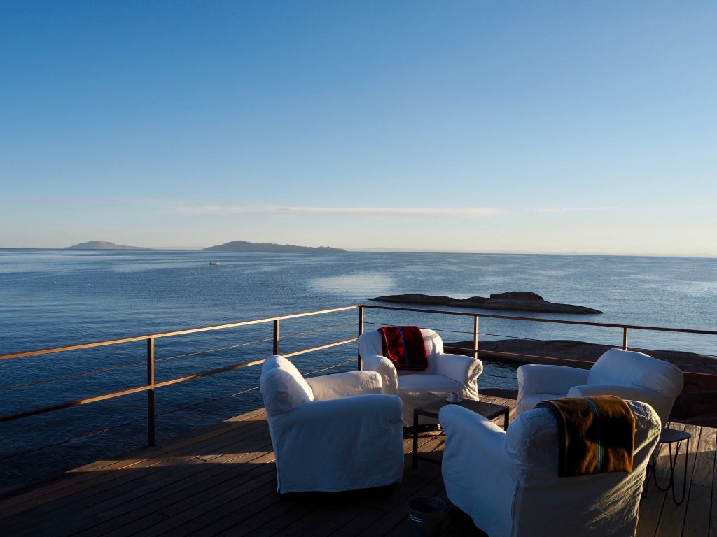 Modern luxury lodge with floor-to-ceiling windows overlooking Lake Titicaca, featuring a stone-paved terrace and contemporary architecture