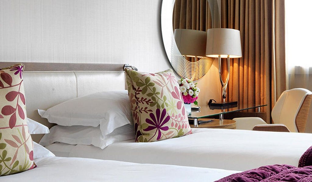 Elegant hotel room with two plush single beds, soft neutral tones, contemporary furnishings, and large window overlooking urban scenset landscape in UK boutique hotel