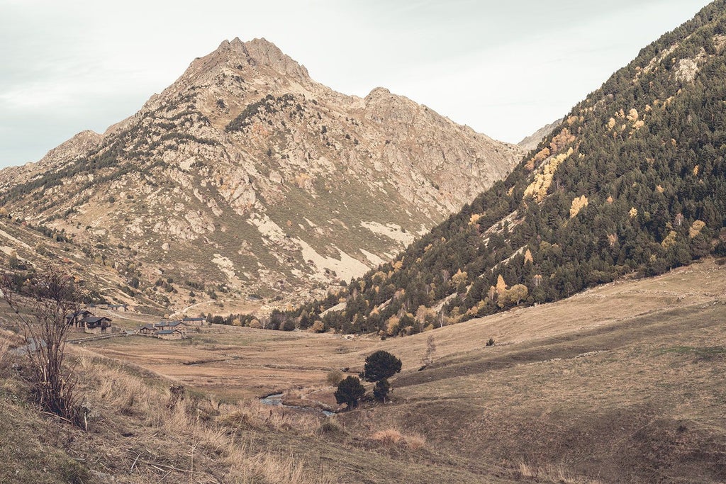 Rustic mountain lodge nestled in scenic Andorra, featuring wood-paneled exterior, snow-capped peaks, and warm alpine lighting against twilight landscape