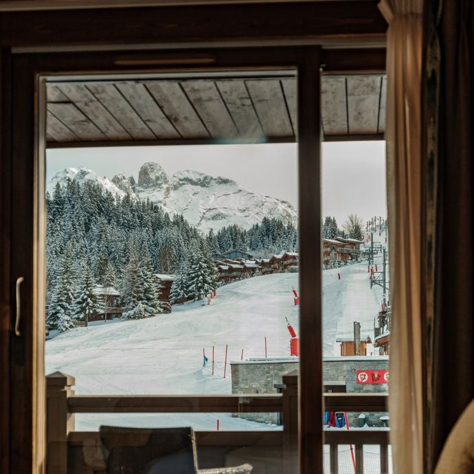 Luxurious alpine hotel room with panoramic mountain views, modern wooden furnishings, and cozy alpine-chic decor overlooking snowy ski slopes in French Alps