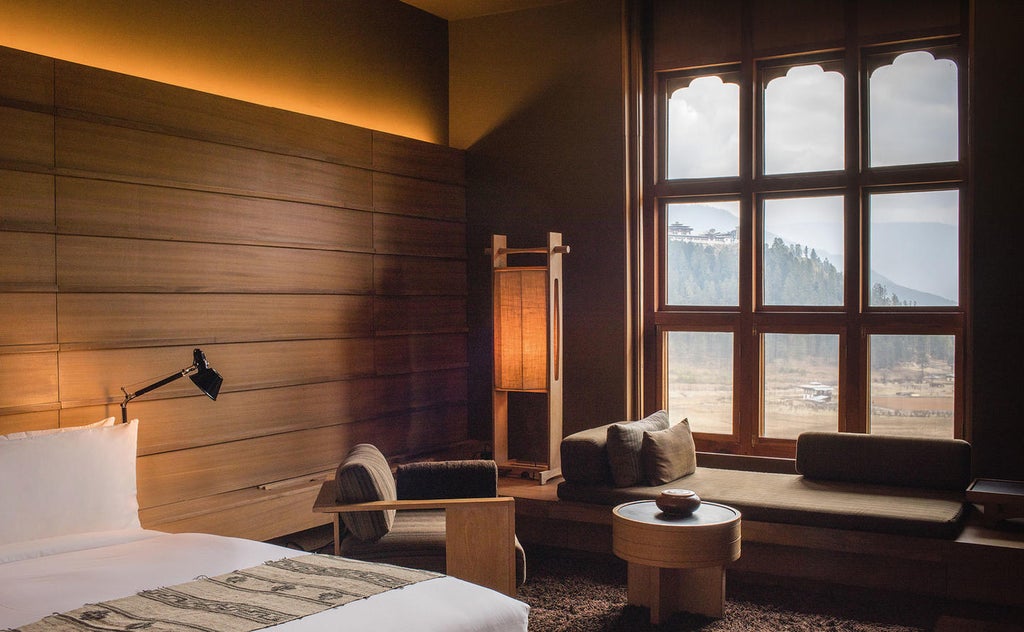 Luxurious mountain lodge with floor-to-ceiling windows offering panoramic views of Bhutan's Gangtey Valley and snow-capped peaks at sunset