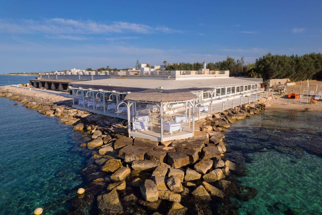 Elegant coastal hotel with infinity pool overlooking azure Mediterranean waters, luxurious terrace, and classic Italian architectural design at scenic scenset location