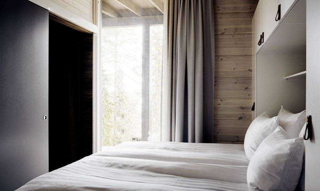 Modern Nordic hotel room with panoramic glass walls, minimalist wooden furniture, and a stunning view of snow-covered pine forest and Arctic landscape at dusk