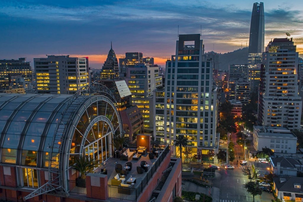 Exterior view of The Ritz-Carlton Santiago featuring elegant stone facade, illuminated entrance with glass canopy and manicured landscaping