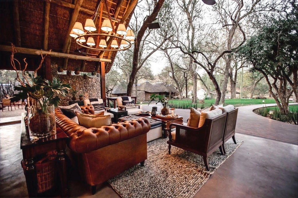 Elegant safari lodge with thatched roof and wooden deck overlooking a serene waterhole in the African bushveld at golden hour