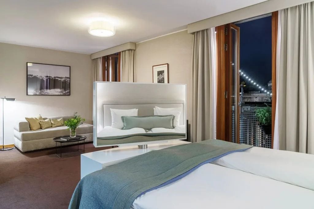 Elegant Swedish hotel room with plush king bed, rich wood furnishings, soft neutral tones, large windows, and sophisticated minimalist design in Berns Hotel