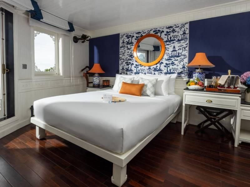 Elegant Au Co Suite aboard Bhaya Cruises with panoramic windows, plush white bedding, and traditional Vietnamese wood furnishings overlooking Halong Bay