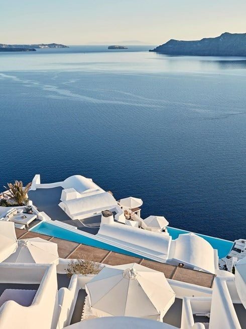 Luxurious white-washed Santorini hotel overlooking deep blue Aegean Sea, featuring traditional Cycladic architecture with cascading infinity pools and pristine terraces.