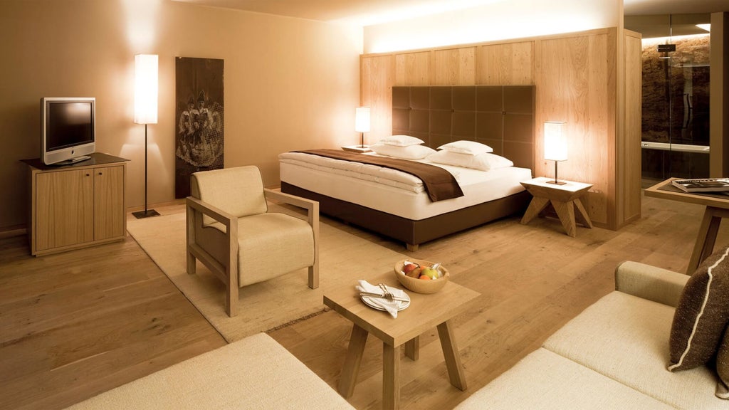 Elegant modern hotel room with floor-to-ceiling windows, private terrace overlooking Dolomite mountains, wood accents, and plush bedding