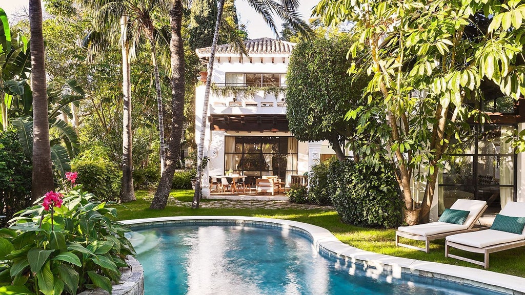 Luxurious beachfront resort with white Mediterranean architecture, palm trees, and azure pool overlooking sparkling coastline of southern Spain