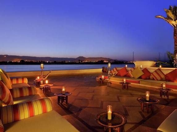 Opulent Hilton Luxor hotel facade with palm-lined infinity pool overlooking the Nile River at sunset, featuring elegant Arabic architecture