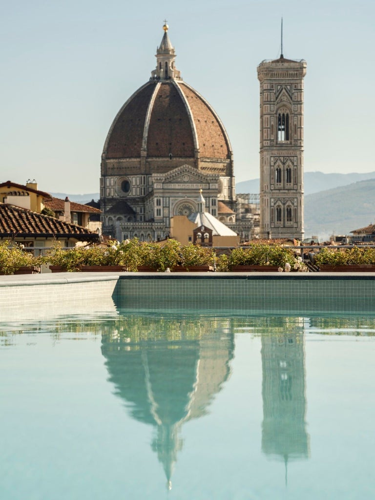 Elegant Tuscan hotel exterior with curved stone archways, terracotta walls, ornate balconies and traditional Mediterranean shutters at sunset