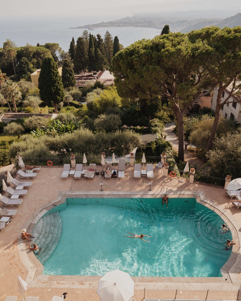 Elegant stone hotel balconies overlook Mount Etna and the Sicilian coastline, with lush Mediterranean gardens and classical architecture