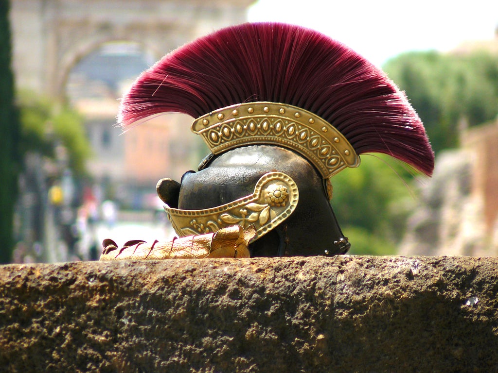 Roman instructor demonstrates sword fighting techniques to tourists while wearing traditional gladiator armor at historic Colosseum grounds