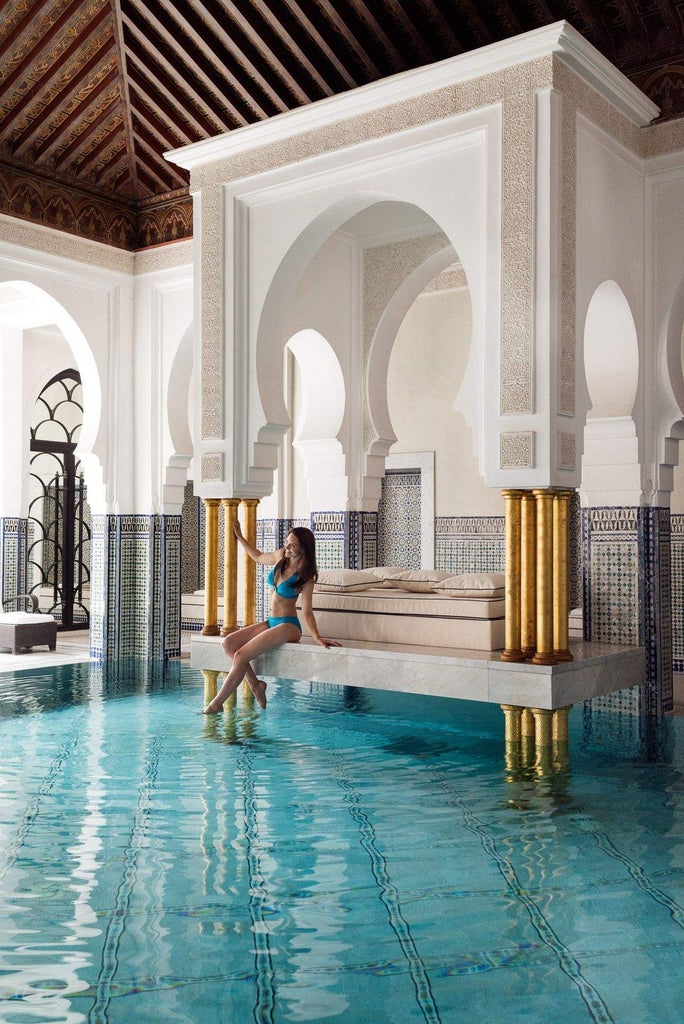 Grand entrance of La Mamounia hotel featuring ornate Moroccan archways, lush garden paths, and traditional geometric tile work in warm hues