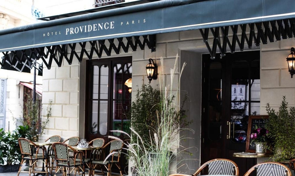 Elegant Parisian boutique hotel exterior with ornate wrought-iron balconies, classic black awnings, and traditional French windows at dusk