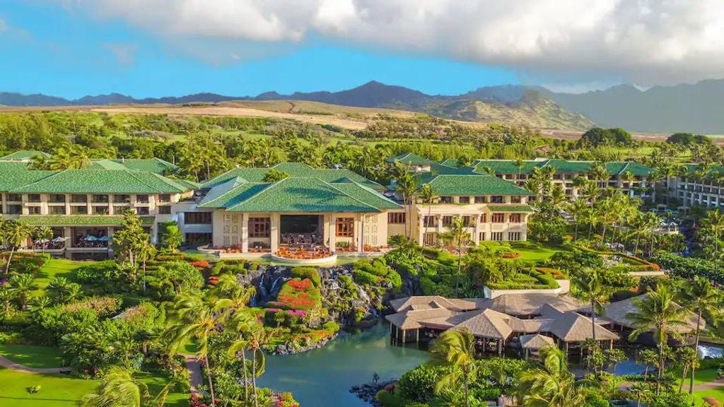 Luxurious Hawaiian beachfront resort with palm trees, grand white facade, multiple swimming pools and lush tropical gardens