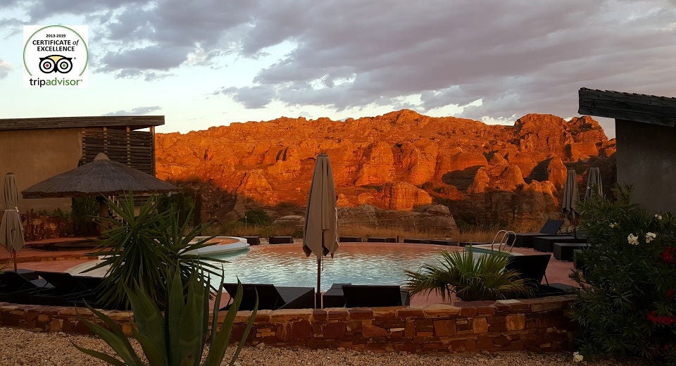 Contemporary stone lodge perched dramatically on rocky cliffs in Madagascar, featuring infinity pool overlooking vast desert landscape