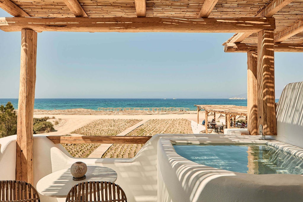 Luxurious beachfront hotel with white-washed walls, azure Aegean waters, and elegant sun loungers on a pristine sandy shoreline in Naxos, Greece.