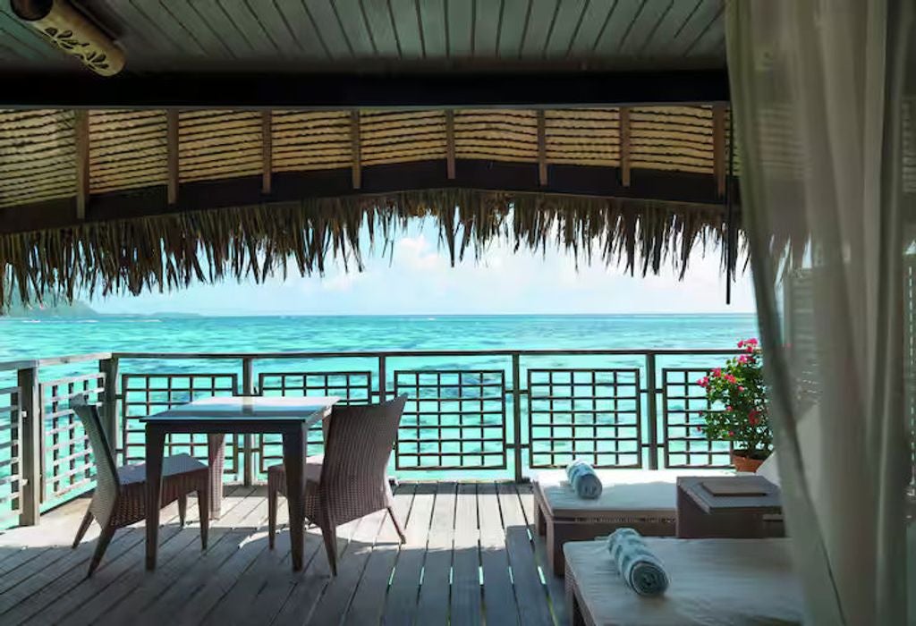 Luxurious overwater villa with private deck, turquoise lagoon views, glass floor panels, and modern Polynesian-style interior furnishings