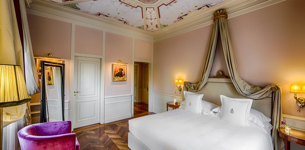 Ornate hotel room with red damask walls, antique gold-framed mirror, crystal chandelier, and plush period furnishings in Florentine style