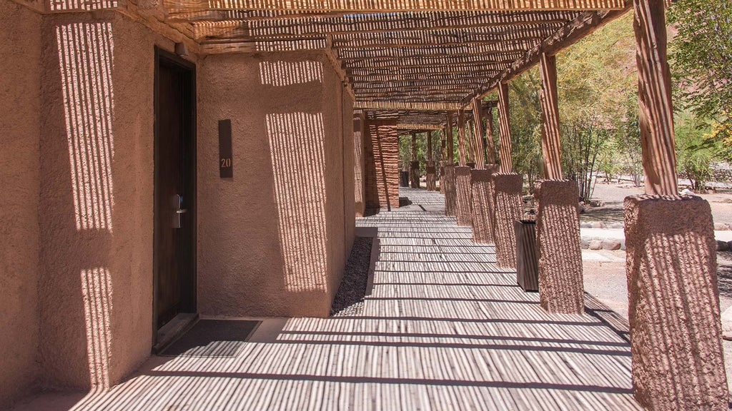 Contemporary desert lodge with adobe walls and wooden terraces nestled against red mountains, featuring an infinity pool at sunset