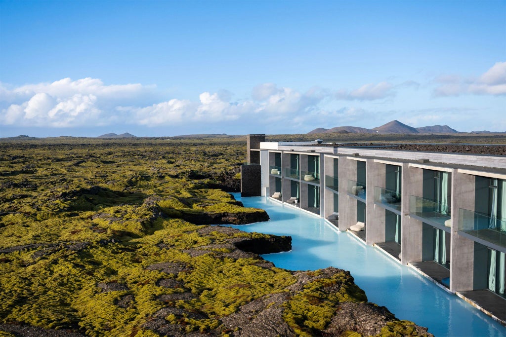 Luxury Nordic hotel nestled against dramatic Icelandic landscape, featuring sleek minimalist architecture with floor-to-ceiling windows overlooking volcanic terrain and mountain silhouettes.