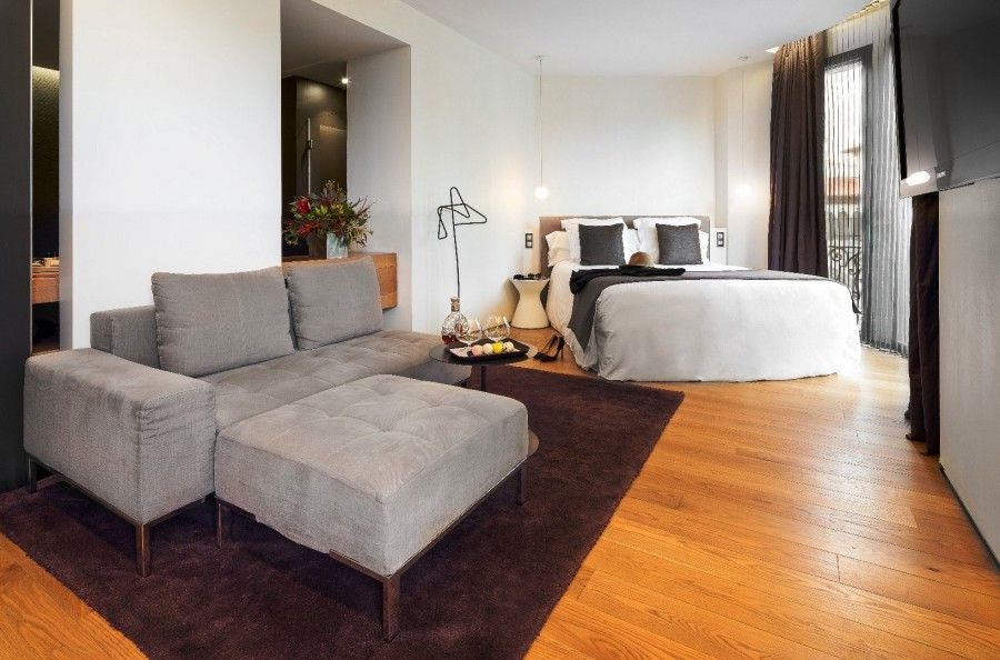 Luxurious hotel suite with panoramic city views, featuring modern design, plush bedding, and expansive floor-to-ceiling windows overlooking Barcelona's skyline