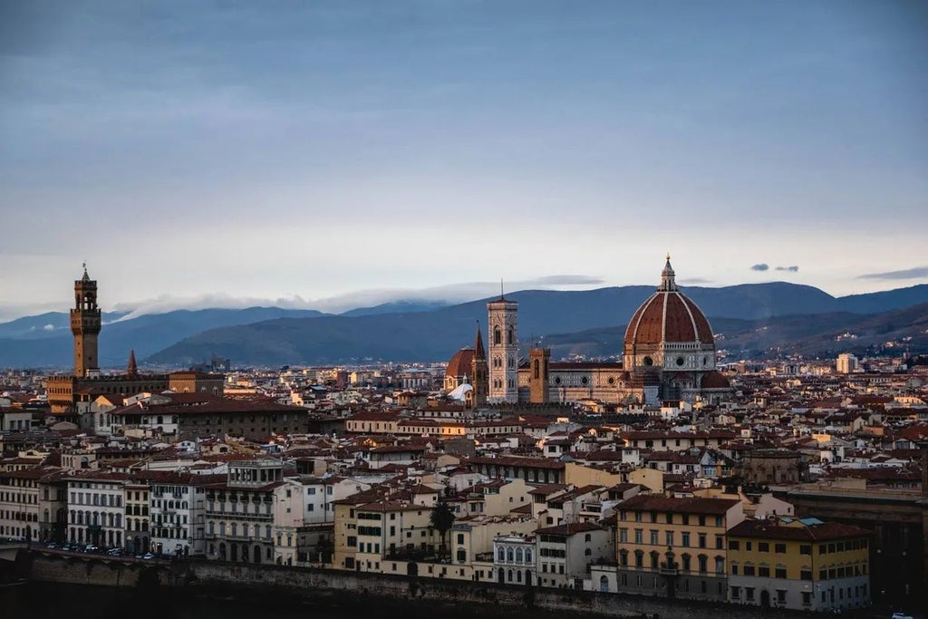 Modern luxury hotel facade in Florence with sleek architectural design, elegant glass exterior, and contemporary urban styling against soft Italian skyline backdrop