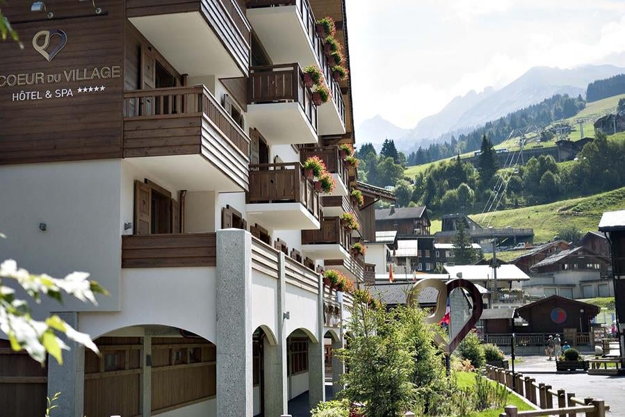 Luxury alpine hotel exterior in snow with wooden balconies, stone facade, and mountain backdrop in La Clusaz, French Alps