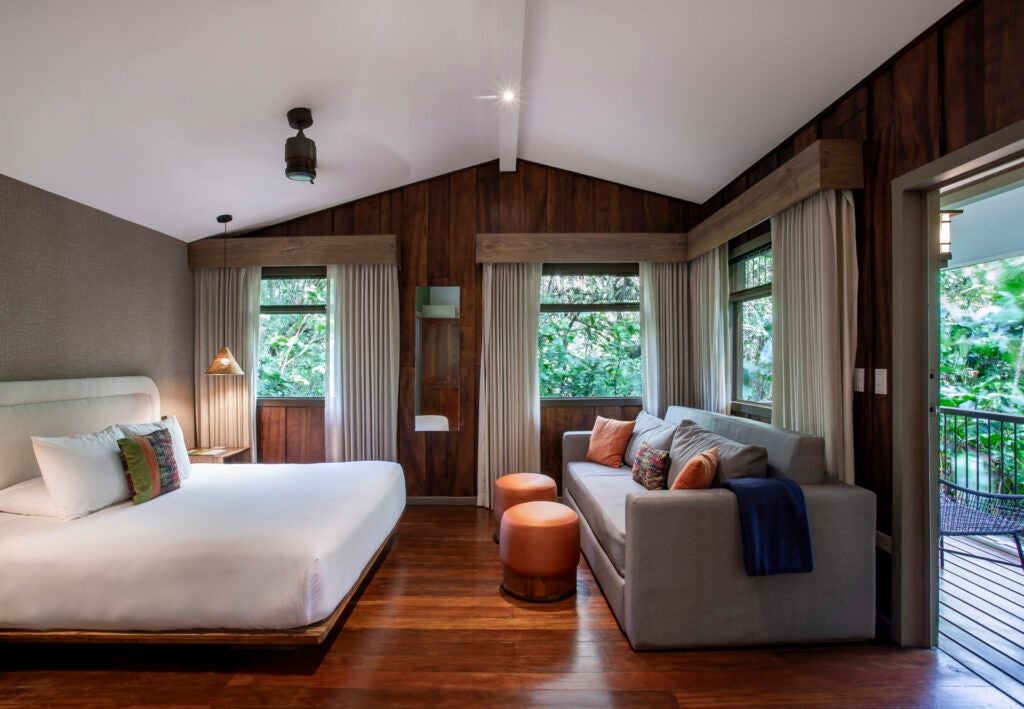 Luxurious wood-paneled superior hotel room at Senda Monteverde with elegant tropical decor, plush bed, and expansive forest view through large windows