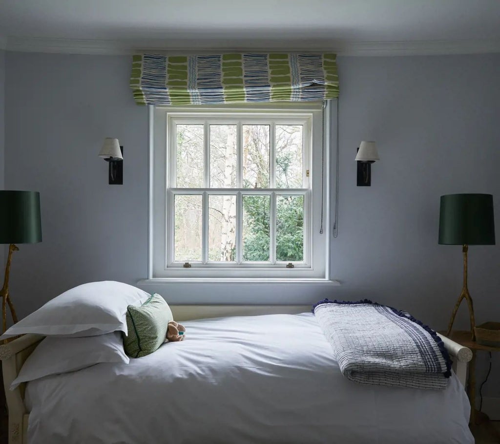 Elegant modern hotel room with forest green walls, plush cream bedding, wooden headboard, and panoramic window overlooking lush countryside scenery