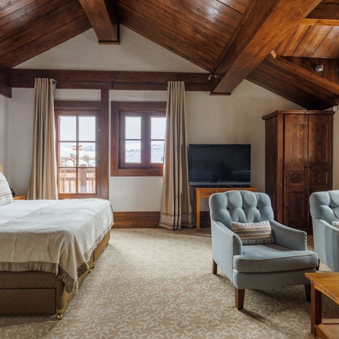 Spacious alpine-style family suite with panoramic mountain valley views, modern alpine furnishings, and warm wooden accents in French mountain resort